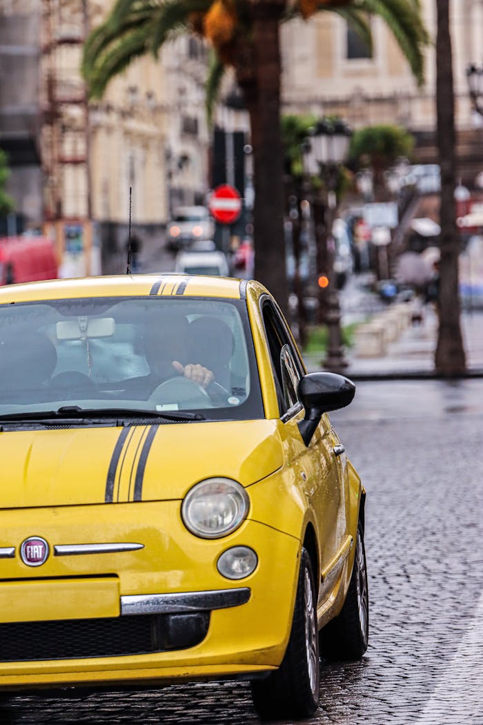 Yellow Fiat 500 cruising rainy Catania street, highlighting vibrant city atmosphere.
